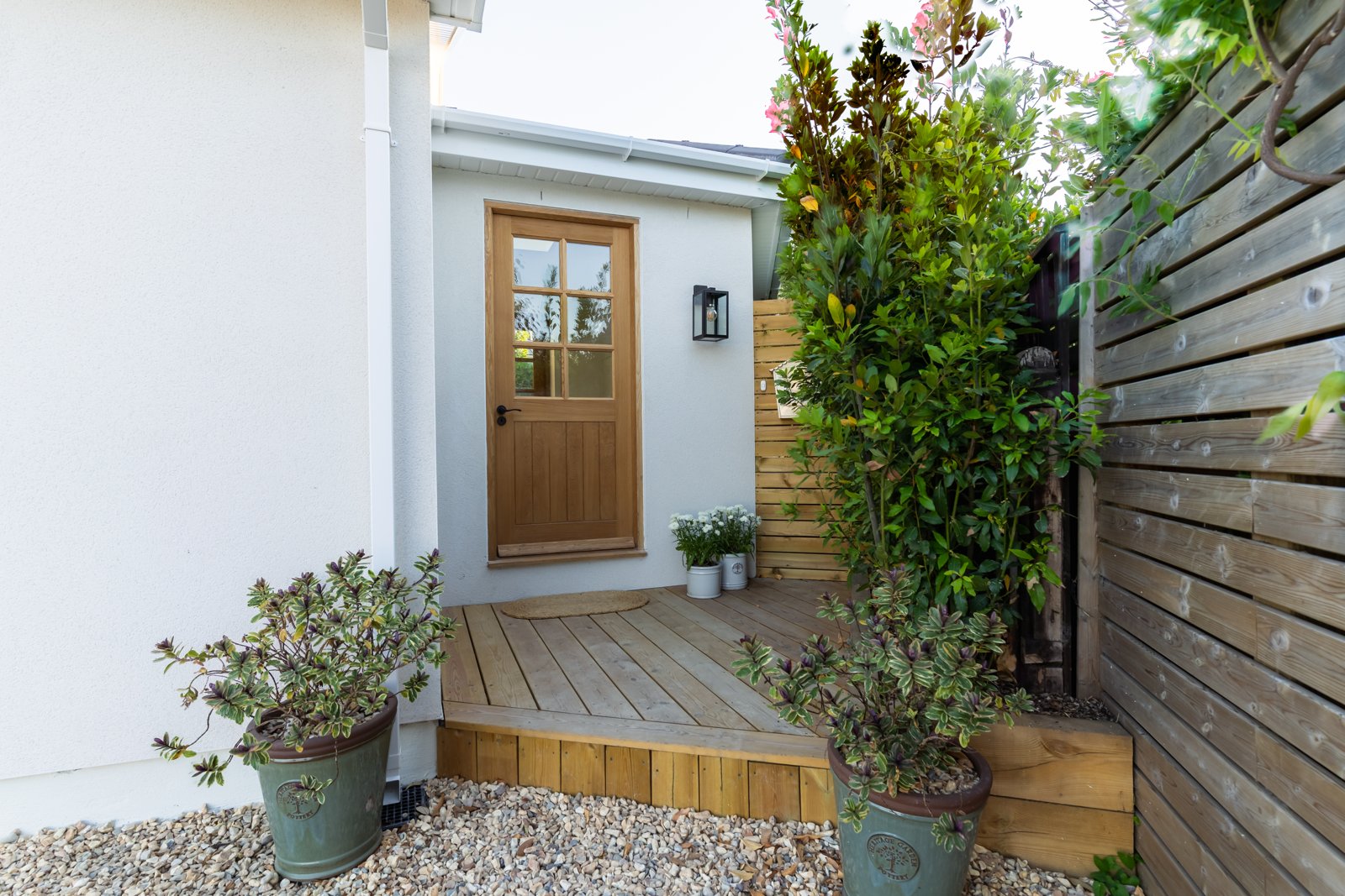 Welcoming wooden front door with decking and potted plants